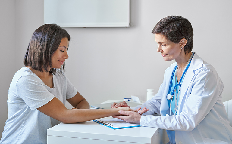 Middle-aged woman doctor in white coat measuring pulse on patient wrist during medical visit