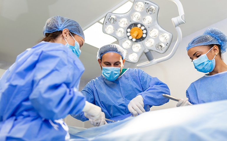 Surgeons doing surgery in operating theatre. Male and female surgeons operating patient. Medical professionals are wearing scrubs.